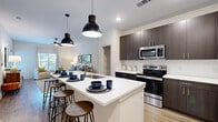 This thoughtfully designed one-bedroom, one-bathroom residence offers a seamless single-floor layout that maximizes comfort and functionality. The open-concept kitchen serves as the centerpiece, featuring dark espresso cabinetry, crisp white countertops, a full suite of stainless steel appliances — including a refrigerator, range, and microwave — and a generous island with pendant lighting and bar seating, making it ideal for both meal prep and casual dining. Light wood-look flooring flows throughout the main living areas, lending warmth and continuity to the space.

The living room is bright and welcoming, benefiting from large windows that invite natural light and offer outdoor views. A ceiling fan adds practical comfort to the airy atmosphere. The bedroom is a restful retreat, fitted with plush carpeting, a ceiling fan, and a large window with serene outdoor views. It connects directly to a dedicated walk-in closet with built-in wire shelving for ample storage.

The bathroom is elegantly finished with dark cabinetry, a white countertop vanity, wood-look tile flooring, and a glass-enclosed walk-in shower. Clean lines and neutral tones throughout the residence create a cohesive, modern aesthetic that is both polished and inviting.