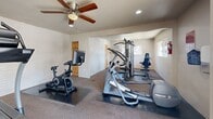 Located at 1611 Madrone Ave in West Sacramento, CA, this dedicated exercise room offers a well-equipped fitness space designed to support a well-rounded workout routine. The room is finished with neutral-toned walls, including a distinctive white painted brick accent wall that adds character to the space, and durable carpet flooring with protective rubber mats placed beneath the equipment.

The fitness area is outfitted with a variety of cardio and strength training equipment, including a Precor elliptical trainer, a treadmill, a stationary spin bike with an integrated display, and a multi-station cable weight machine suitable for a range of strength exercises. A dedicated bench and additional seated equipment provide further options for resistance training.

A large wall-mounted mirror runs along one side of the room, visually expanding the space and allowing users to monitor their form during workouts. Recessed lighting and a ceiling fan with a light fixture ensure the room remains well-lit and properly ventilated. Natural light enters through windows on two walls, creating a bright and energizing atmosphere.

Safety features include a mounted fire extinguisher and posted room rules signage. A wall-mounted air conditioning unit provides additional climate control. Access to the room is provided through a solid wood door, and the space benefits from a clean, organized layout that maximizes functionality.
