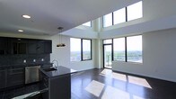 Located at 240 S Harrison St in East Orange, NJ, this sophisticated two-floor residence makes a bold architectural statement through its dramatic vertical design and modern aesthetic. The open-plan living and kitchen area immediately commands attention with its soaring double-height ceilings and expansive floor-to-ceiling windows that flood the interior with natural light from multiple directions. Rich, dark hardwood flooring runs throughout, providing a warm contrast to the crisp white walls and contemporary finishes.

The kitchen is sleek and well-appointed, featuring dark cabinetry, a granite countertop island with an integrated sink, a modern pendant light fixture, and a chic tile backsplash — all designed with both style and function in mind. The living area flows seamlessly toward a balcony, offering direct access to sweeping panoramic views of the East Orange and greater Essex County skyline, with lush treetop scenery stretching into the horizon.

Upper clerestory windows amplify the sense of openness, drawing in additional daylight and enhancing the airy, loft-like atmosphere of the space. Spanning two floors, the layout provides a thoughtful separation between living and private areas. The overall ambiance is one of urban sophistication — modern, light-filled, and elevated in every sense.