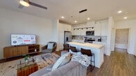 This well-appointed two-story home offers 3 bedrooms and 3 bathrooms across two thoughtfully designed floors. The main level centers around an open-concept kitchen and living area, where clean lines and modern finishes create a cohesive, contemporary atmosphere. The kitchen is equipped with white shaker-style cabinetry reaching to the ceiling, stainless steel appliances including a French door refrigerator and range, a tile backsplash, and a large island with a white countertop and bar seating — ideal for casual dining or entertaining. The adjacent living area is bathed in natural light from oversized windows and features warm wood-look flooring that flows consistently throughout both floors. Upstairs, the primary bedroom offers a comfortable retreat with ample natural light, a ceiling fan, and access to a generously sized walk-in closet outfitted with built-in shelving and dual hanging rods. The additional bedrooms are well-proportioned with bright windows. The bathrooms are finished with marble-look tile surrounds, white vanities, and wood-look flooring. One bathroom features both a soaking tub and a separate glass-enclosed shower. Three staircases provide convenient internal circulation. The overall design is clean, bright, and modern throughout.
