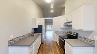 Located at 7002 N Colton St in Spokane, WA, this single-floor residence offers a well-maintained interior with a cohesive, updated aesthetic throughout. The living room immediately impresses with its dramatic vaulted ceilings that lend an open, airy quality to the space. Rich wood-style flooring runs throughout, complementing the neutral gray walls. A tile-surround fireplace serves as a focal point on one wall, while a large sliding glass door with vertical blinds fills the room with natural light and provides outdoor access. A wall-mounted air conditioning unit adds practical comfort.

The galley-style kitchen is efficiently designed with white shaker cabinetry, gray countertops, and a mosaic tile backsplash. Stainless steel appliances—including a refrigerator, electric range, and dishwasher—complete the space, which opens toward the living area for a connected feel.

The bedroom features a large window with outdoor views of mature trees, a baseboard heater, and a sliding-door closet with built-in shelving. The bathroom includes a single-sink vanity with gray countertop, a large mirror, tiled accent wall detail, and a full tub-shower combination. The overall ambiance is clean, bright, and move-in ready.