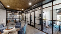 Located at 401 Lime Quarry Rd in Madison, Alabama, this single-floor amenity space showcases a sophisticated blend of contemporary design and functional communal areas. The interior is defined by bold architectural choices, including floor-to-ceiling black-framed glass partition walls that divide distinct zones while maintaining an open, transparent feel throughout.

The lounge area greets visitors with plush blue upholstered seating, warm wood-look tile flooring, and a striking textured cork ceiling that adds natural depth and warmth. A decorative laser-cut metal screen serves as an artistic room divider, further elevating the visual character of the space.

Adjacent to the lounge, a dedicated library and meeting room features a coffered dark ceiling, a built-in wood shelving unit with a Murphy-style bench, patterned area rugs, and a central conference table with upholstered chairs — ideal for collaborative work or private gatherings. A separate glass-enclosed workspace, labeled "Library," offers natural light from exterior windows and ample room for focused work.

The mail and lobby area includes a large bank of individual mailboxes set against a dark shiplap-clad architectural column, complemented by light hardwood flooring. A clean, bright flex room adorned with circular acoustic wall panels provides a minimalist, versatile space suitable for various uses. Together, these areas form a well-appointed, design-forward community hub.