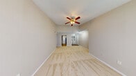 This single-story residence offers a thoughtfully arranged floor plan with interconnected living spaces finished in neutral tones throughout. The main living area is spacious and open, featuring soft carpeting, vaulted ceilings, and a ceiling fan with a light kit. Natural light enters through a large window, creating a bright and welcoming atmosphere. A half-wall partition separates the living area from the kitchen, which features a pass-through granite countertop bar. The galley-style kitchen is well-appointed with dark espresso cabinetry, granite countertops, stone tile backsplash, black appliances including an electric range and refrigerator, a stainless steel sink, and wood-look flooring. Multiple bedrooms are carpeted and include ceiling fans and windows with blinds. The primary bedroom connects directly to a bathroom that features dark cabinetry, a granite vanity top, a large mirror, and wood-look flooring. The full bathroom includes a tub and shower combination with white tile surround. Additional rooms provide flexible space, and textured ceilings are consistent throughout the residence.