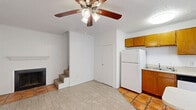 This two-story home efficiently distributes its living space across two floors, connected by a carpeted staircase with a classic white baluster railing. The ground floor hosts an open-plan kitchen and living area, finished with light-toned tile flooring and a ceiling fan with integrated lighting. The kitchen is well-appointed with warm wood cabinetry, white appliances including a refrigerator and electric range, a single-basin sink, and a peninsula counter that provides additional prep and dining space. A window brings in natural light, keeping the kitchen bright and functional. The full bathroom on this level features terracotta tile flooring, a tiled tub/shower surround, a vanity with wood cabinetry, and overhead storage. Upstairs, the spacious bedroom is carpeted and includes two closets—one with classic paneled double doors—a ceiling fan, and a window with blinds that admits natural light. A wall-unit air conditioner ensures year-round comfort. The textured ceilings are consistent throughout the home, lending a cohesive character to each room. With its practical layout and functional finishes, this home offers a straightforward and comfortable living environment.