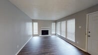 This single-floor residence offers a thoughtfully designed layout with a blend of functional spaces and modern finishes. The expansive living room serves as the centerpiece of the home, highlighted by a classic fireplace framed by a clean white mantel and surround. Multiple windows dressed with white horizontal blinds allow generous natural light to fill the room, complementing the rich, dark hardwood-style flooring that extends throughout the space. The textured ceiling adds a subtle architectural detail consistent across the entire residence.

The kitchen is well-equipped and stylish, featuring dark espresso cabinetry paired with striking dark granite countertops that carry a bold, contrasting aesthetic. Stainless steel appliances, including a dishwasher and electric range with an over-the-range microwave, provide modern convenience. A breakfast bar peninsula creates a natural division between the kitchen and adjacent living areas, making the space ideal for both cooking and entertaining.

The hallway connects the main living areas to the private spaces, including a bathroom that echoes the kitchen's design language with a dark vanity, granite countertop, and a walk-in shower with white tile surround. Wood-look flooring continues throughout, tying the home together with a cohesive and contemporary feel. Ceiling fans in the secondary areas add comfort and practicality to this well-rounded residence.