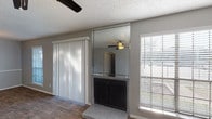 This single-story space is thoughtfully laid out, with distinct zones for living, cooking, sleeping, and bathing. The living room serves as the central gathering area, highlighted by a fireplace framed with a floor-to-ceiling mirrored surround that adds visual depth to the room. Wood-look flooring runs throughout the main living areas, reflecting natural light that streams in through multiple windows fitted with horizontal blinds. A sliding glass door with vertical blinds provides outdoor access and additional light. A ceiling fan keeps the space comfortable year-round, and a textured ceiling is consistent throughout.

The kitchen is galley-style, featuring dark espresso cabinetry, speckled laminate countertops, a stainless steel sink, and black appliances including a refrigerator and electric range. An open pass-through connects the kitchen to the adjacent dining and living areas.

The bedrooms are carpeted and finished in neutral gray tones, each equipped with ceiling fans or flush-mount lighting and windows that allow natural light. Both bathrooms feature wood-look flooring, dark vanity cabinetry with speckled countertops, full tub-shower combinations with white tile surrounds, and overhead lighting with mirrored storage above the vanities.