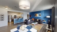This single-floor residence is thoughtfully designed with a bold, modern aesthetic and an open-concept layout that seamlessly connects the living, dining, and kitchen areas. The living room is a standout space, anchored by a striking cobalt blue accent wall, a large sectional sofa, and a colorful area rug that adds energy and warmth. Multiple windows bathe the area in natural light, while a textured ceiling and a prominent overhead light fixture add architectural character. The dining area flows naturally from the living space, offering a comfortable setting for gatherings.

The kitchen is well-appointed with two-tone cabinetry — crisp white upper cabinets paired with charcoal lower cabinets — complemented by light quartz countertops, a classic white subway tile backsplash, and a full suite of stainless steel appliances. A peninsula with bar seating enhances both functionality and social connectivity.

The bedrooms each carry their own distinct personality, with accent walls in shades of blue and warm neutral tones. One bedroom features a serene, warm-toned palette highlighted by decorative macramé wall art. The bathrooms are functional and clean, featuring warm wood vanities, framed mirrors, tile flooring, and accessibility grab bars. Hardwood-style flooring runs throughout the main living areas, unifying the space with a cohesive, contemporary feel.