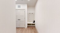 This well-designed 2-bedroom, 2-bathroom single-floor residence offers a cohesive, modern aesthetic characterized by crisp white walls, light wood-style flooring, and contrasting black hardware details carried consistently throughout the space. The open-concept kitchen features white shaker cabinetry, a hexagonal tile backsplash, stainless steel appliances, and a window that brings in natural light. The adjoining dining area is brightened by dual windows with outdoor views, creating an inviting setting. The living room offers a comfortable, relaxed atmosphere, complete with a ceiling fan and ample space for furnishings. The primary bedroom is a well-proportioned retreat featuring a ceiling fan, a window, and direct access to a dedicated walk-in closet outfitted with built-in shelving and dual hanging rods. The second bedroom is bright and functional, also benefiting from natural light via a window and ceiling fan. A hallway mudroom area provides a built-in bench with open cubbies, beadboard paneling, and wall hooks for organized entry storage, alongside a set of double shaker-style doors leading to a closet. The bathroom is finished with marble-look tile surround, white cabinetry with black pulls, and wood-style flooring, maintaining the home's clean, contemporary character.
