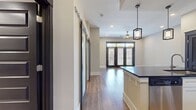 This efficiently designed 670 square foot single-story residence maximizes its compact footprint with a thoughtful layout. The heart of the home is an open-concept space combining the kitchen and living room, promoting a seamless flow for daily activities and entertaining. A standout feature is the set of three French doors, framed by dark wood, which flood the interior with natural light and offer views to the outside. These doors are topped with transom windows, enhancing the sense of height and airiness in the room. The flooring throughout is a warm, wood-look material that adds a touch of rustic charm while ensuring durability. Recessed lighting in the ceiling provides even illumination, complemented by a modern ceiling fan for comfort. The neutral-toned walls create a blank canvas for personalization, while the clean lines and minimalist design contribute to a contemporary aesthetic. This space efficiently incorporates all essential living areas, including a separate bathroom and laundry facilities, making it an ideal setup for compact urban living or as a guest house.