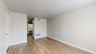 This two-floor residential space offers a clean, functional layout with a neutral color palette throughout. The main living areas feature light hardwood-style flooring that flows seamlessly from room to room, complemented by crisp white baseboards and textured ceilings. Large windows fitted with blinds allow natural light to fill the space, creating a bright and welcoming atmosphere.

The entry area opens into a spacious living room with warm flooring and ample wall space, leading into additional rooms with ease. A secondary living or dining area is visible beyond, maintaining the same light, airy aesthetic with a view toward exterior greenery.

The kitchen is equipped with dark cabinetry extending to the ceiling, providing generous storage, along with a full suite of black appliances including a range with overhead ventilation and a dishwasher. Light countertops and a stainless steel sink complete the practical workspace.

The bedrooms are carpeted in a neutral, speckled pattern, offering comfort underfoot. Each room benefits from natural light through slatted blinds, with sufficient wall space for versatile furniture arrangements.

The bathroom features full white tile surround on the tub-shower combination, paired with wood-style flooring, offering a clean and functional finish throughout.