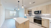 Located at McEwen Rd in Farmers Branch, TX, this well-appointed one-bedroom, one-bathroom residence offers a thoughtfully designed layout across a single floor. Light wood-tone flooring flows consistently throughout the space, creating a cohesive and clean aesthetic. The open-concept kitchen and living area serves as the heart of the home, showcasing natural wood cabinetry, white quartz countertops, a grey subway tile backsplash, and a full suite of stainless steel Whirlpool appliances, including a refrigerator with ice maker, electric range, and over-the-range microwave. A kitchen island provides additional prep and seating space. The bedroom is comfortably sized, featuring a ceiling fan, blinds that allow for natural light and privacy, and direct access to the bathroom. The bathroom is finished with light wood cabinetry, a glass-enclosed walk-in shower with tile surround, and direct access to a dedicated walk-in closet with built-in shelving. Crisp white walls and black hardware accents are carried throughout, lending a modern, minimalist character to the entire residence. Ceiling fans in the main living areas and bedroom add both function and style to this clean, contemporary home.