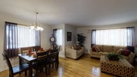 This two-story home offers two bedrooms and two bathrooms across a generously sized floor plan. The main living area features an open-concept layout that seamlessly connects the dining and living spaces, creating a comfortable and functional environment for everyday living and entertaining. Warm hardwood flooring extends throughout the main level, adding a classic, inviting aesthetic to the space.

The dining area is illuminated by a chandelier and benefits from abundant natural light streaming through multiple windows dressed with sheer and decorative curtains. This area comfortably accommodates a full dining set, making it ideal for gatherings. The adjacent living room is equally well-lit, with additional windows providing bright, airy ambiance. The neutral wall tones throughout create a versatile backdrop that complements a variety of décor styles.

The two-story layout offers distinct separation between living areas, lending privacy and defined functionality to each floor. Overall, the home presents a well-balanced combination of open communal spaces and private quarters, making it a practical and comfortable residence.