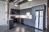 This single-floor loft in Memphis, Tennessee offers a compelling fusion of industrial heritage and contemporary design. Polished concrete floors run throughout the entire unit, lending a sleek, cohesive aesthetic that complements the space's raw architectural elements. Exposed structural columns—some bearing traces of the building's original patina—serve as striking design features that reinforce the loft's industrial character.

The kitchen is a standout area, outfitted with slate-blue cabinetry that extends nearly to the ceiling for ample storage, a light stone-topped peninsula ideal for casual dining or meal prep, and a full suite of stainless steel appliances including a range, microwave, dishwasher, and refrigerator. A white subway tile backsplash adds a clean, modern contrast to the bold cabinetry.

The bedroom is generously proportioned with soaring ceilings, a walk-in closet, and an original column detail that adds character. The bathroom features a contemporary vanity with dark cabinetry, a mirror, and a full-size tub, maintaining the unit's clean, minimalist palette. A hallway with natural light from oversized windows connects the living areas, while exposed ductwork on the ceiling further enhances the loft's urban industrial ambiance throughout.