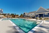 Located at 1551 Riverside Pkwy in Douglasville, Georgia, this outdoor amenity space centers around a generously sized, crystal-clear swimming pool that serves as the focal point of a well-appointed resort-style retreat. The pool features elegant tiled accents, wide entry steps, and multiple access points including stainless steel handrails, accommodating swimmers of all levels with both shallow and deeper sections clearly marked.

Surrounding the pool, a broad, light-toned concrete sundeck provides ample space for relaxation, lined with rows of cushioned lounge chairs and occasional umbrella-shaded seating areas for added comfort. The deck's layout encourages both sunbathing and social gatherings, with thoughtfully arranged furniture clusters that offer versatility for residents.

The space is framed by a striking tiered stone retaining wall that adds architectural texture and definition to the area, while manicured landscaping and freshly planted greenery introduce natural warmth. A charming clubhouse building finished in navy blue board-and-batten siding with a peaked roof anchors one end of the pool area, complementing the overall aesthetic. Pergola structures and additional shaded lounging zones complete the outdoor experience. Under open Georgia skies, this pool area delivers a vibrant, well-designed environment ideal for leisure and community living.
