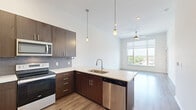 Located at 11501 W 81st St in Lenexa, KS, this well-appointed one-bedroom, one-bathroom unit offers a thoughtfully designed open-concept layout with contemporary finishes throughout. The combined kitchen and living area serves as the heart of the space, showcasing soaring ceilings, warm wood-look flooring, and a large window that fills the room with natural light and outdoor views. The kitchen is outfitted with rich dark-walnut cabinetry, a quartz countertop peninsula, a full suite of stainless steel appliances including a French door refrigerator, electric range, microwave, and dishwasher, plus a stylish tile backsplash and pendant lighting overhead. A ceiling fan in the living area adds both comfort and character. The spacious bedroom features plush carpet, a generous closet, and a large window with scenic views. The bathroom is elegantly finished with a dual-sink quartz vanity, dark wood cabinetry, a wide mirror, and a tiled soaking tub and shower combination. Recessed lighting and brushed nickel fixtures lend a clean, modern aesthetic throughout. The overall ambiance is bright, contemporary, and move-in ready.