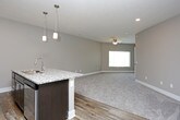 This single-floor unit is designed with a cohesive, contemporary aesthetic that balances functionality and style throughout its living spaces. The kitchen serves as a focal point, showcasing rich dark cabinetry paired with speckled granite countertops and a suite of stainless steel appliances, including a refrigerator, electric range, and over-the-range microwave. A kitchen island with a built-in sink provides additional workspace and doubles as a casual dining or gathering area, illuminated by pendant lighting overhead. Wood-look flooring in warm, varied tones runs throughout the kitchen, adding texture and visual warmth.

The living area transitions seamlessly from the kitchen and is finished with plush wall-to-wall carpeting in a neutral tone, offering a comfortable and versatile space. Neutral gray walls, recessed lighting, and a ceiling fan contribute to a clean, practical environment. Multiple electrical outlets are positioned along the walls, providing flexibility for furniture arrangement.

The bathroom is well-appointed with the same wood-look flooring found in the kitchen, creating continuity throughout the unit. A full-size soaking tub with a shower combination is fitted with a curved curtain rod, while a dark-stained vanity with granite countertop and an integrated sink rounds out the space with consistent, polished finishes.