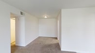 This single-story unit offers a practical and straightforward layout featuring two bedrooms, one bathroom, and an additional den that provides flexible space for a home office, reading nook, or extra storage. The interior is finished with neutral white walls and wall-to-wall carpeting in a warm beige tone, creating a clean and understated aesthetic throughout. The main living area is open and well-proportioned, with ceiling-mounted lighting providing consistent illumination. A ceiling vent ensures climate control comfort year-round. The white walls and simple trim work give the space a bright, airy feel that serves as a blank canvas for personalization. Doorways connect the main areas in a logical flow, contributing to the unit's overall ease of navigation. The den adds notable versatility to the floor plan, distinguishing this unit from standard two-bedroom layouts. Overall, the space presents a no-frills, move-in-ready environment with a cohesive neutral palette suited to a variety of furnishing styles and lifestyle needs.