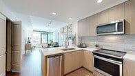 Located at 310 A St in San Diego's vibrant East Village neighborhood, this single-floor residence offers a thoughtfully designed open-concept layout with modern finishes throughout. The kitchen serves as a central feature, outfitted with light wood cabinetry, a tile backsplash, white quartz countertops, and a full suite of stainless steel appliances, including a side-by-side refrigerator, range, microwave, and dishwasher. A peninsula with seating connects the kitchen seamlessly to the dining and living areas, where large floor-to-ceiling windows flood the space with natural light and offer views of the surrounding cityscape. Wood-style flooring extends throughout the main living areas and hallway, lending warmth and visual continuity. The bedroom is a calm, well-proportioned retreat, complemented by a private bathroom featuring marble-style tile flooring, a floating wood vanity with a white countertop, and a large mirror. An adjacent walk-in closet provides generous built-in shelving and hanging storage. A dedicated laundry area is conveniently accessible from the hallway. Recessed lighting throughout maintains a clean, polished aesthetic across the entire residence.