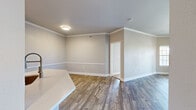 This single-story, 3-bedroom, 2-bathroom home offers a thoughtfully designed layout that balances comfort and functionality. The open-concept living, dining, and kitchen area serves as the heart of the home, featuring warm wood-look flooring, crown molding, and neutral-toned walls throughout. The living room is highlighted by a classic fireplace, a ceiling fan, and a sliding glass door that opens to a private balcony, framed by flanking windows that invite natural light and outdoor views.

The modern kitchen is equipped with stainless steel appliances, white cabinetry, a tile backsplash, track lighting, and a peninsula island with a double sink and light quartz countertops — ideal for both cooking and casual dining.

The primary bedroom is a generously sized retreat featuring plush carpet, an arched window, a ceiling fan, and access to a private en-suite bathroom. The en-suite includes a soaking tub with tiled surround, a white vanity with quartz countertop, and wood-look flooring. Two additional bedrooms offer carpeted floors and ample natural light. Closets feature wire shelving for organized storage. A hallway connects the bedrooms, with a second full bathroom conveniently accessible. The home presents a clean, move-in-ready aesthetic throughout.