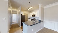 This single-story residence offers a thoughtfully designed layout featuring three bedrooms, two bathrooms, and two closets. The open-concept kitchen and living area serves as the heart of the home, where the kitchen stands out with crisp white shaker-style cabinetry, a classic subway tile backsplash, sleek gray countertops, and stainless steel appliances including a range, microwave, and refrigerator. A peninsula with a double sink provides additional workspace and casual seating potential, while wood-look flooring anchors the area with warmth and durability. The spacious primary bedroom is highlighted by a ceiling fan, large windows that invite natural light and outdoor views, and crown molding that adds an elegant finishing touch. A walk-in closet with built-in wire shelving systems offers generous storage. The secondary bedrooms are well-proportioned, featuring soft carpeting and natural light from sizable windows. Both bathrooms are finished with wood-look flooring, white vanity cabinetry with gray countertops, and one includes a full soaking tub and shower combo. Neutral tones and consistent trim details throughout create a cohesive, clean aesthetic that lends itself well to a variety of interior styles.