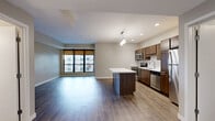 Located on the third floor at 1400 Walnut St in downtown Des Moines, Iowa, this one-bedroom, one-bathroom unit offers a well-designed layout with modern finishes throughout. The open-concept kitchen and living area serves as the heart of the unit, featuring warm wood cabinetry, stainless steel appliances including a range, microwave, and refrigerator, a white subway tile backsplash, and a central island with a white countertop and pendant lighting above — ideal for both cooking and casual dining. Hardwood-style flooring extends through the main living areas, adding warmth and continuity to the space. The living area is bright and open, with large windows framing views of the surrounding cityscape and allowing generous natural light to fill the room. The bedroom is a comfortable, carpeted retreat with soft neutral tones, offering a quiet and practical space. A closet provides convenient storage. The bathroom is clean and functional, featuring a soaking tub and shower combination with white tile surround, wood-toned cabinetry, and hardwood-style flooring that ties in with the rest of the unit. Neutral wall colors and consistent finishes throughout create a cohesive, modern aesthetic suited for urban living in the heart of Des Moines.