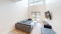 Located on Patrick Henry Drive in Blacksburg, Virginia, this contemporary two-floor residence offers a clean, modern aesthetic throughout. Light wood-look flooring runs consistently across both levels, complementing the neutral white and beige walls that create a bright, cohesive atmosphere.

The main level showcases a dramatic living area with soaring double-height ceilings and a striking wall of clerestory windows that flood the space with natural light. French doors open directly to the outdoors, enhancing the sense of openness. The kitchen is thoughtfully designed with sleek flat-front cabinetry in white and light wood tones, stainless steel appliances including a full-size refrigerator and range, recessed lighting, and ample counter space.

The upper level houses well-proportioned bedrooms, each furnished with a bed with built-in storage, a desk, and ergonomic chair — practical for study and rest. Large windows in the bedrooms invite natural light and outdoor views. Bathrooms are finished in a minimalist style with light wood vanities, clean white walls, wood-look flooring, and accessibility grab bars in select bathrooms.

Additional rooms on the upper level offer flexible use, featuring track lighting, double-door closets, and windows overlooking the surrounding neighborhood. The thoughtful two-level layout balances communal living spaces with private retreats throughout.