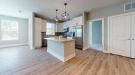 Located at 8400 Palmetto Commerce Pkwy in Ladson, South Carolina, this single-floor residence offers a thoughtfully designed open-concept layout with modern finishes throughout. The heart of the home is a well-equipped kitchen featuring crisp white shaker cabinetry, granite countertops, a herringbone-patterned tile backsplash, and a full suite of stainless steel appliances. A central island with pendant lighting provides additional prep space and serves as a natural gathering point, flowing seamlessly into the adjacent living and dining areas, which are finished with warm wood-look flooring. The bedrooms are carpeted for comfort, with large windows fitted with white blinds that allow generous natural light and outdoor views. The primary bathroom is spacious, offering a double-sink vanity with granite countertops, white cabinetry with matte black hardware, a walk-in tiled shower, and light wood-look flooring. A secondary bathroom mirrors the same refined aesthetic with a single vanity and tub-shower combination. Neutral gray walls and clean white trim are consistent throughout, lending the space a cohesive, contemporary ambiance. The overall design balances practicality with modern style, making it a functional and attractive single-level home.