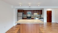 This contemporary two-floor residence offers a thoughtfully designed open-concept layout that seamlessly connects the living, dining, and kitchen areas. The main living space is anchored by warm hardwood flooring that extends throughout, a built-in linear fireplace, and multiple windows that invite generous natural light. Exposed industrial-style conduit and track lighting add a modern edge to the clean, neutral-toned interiors.

The kitchen is a standout feature, equipped with a full suite of stainless steel appliances including a refrigerator, range, microwave, and dishwasher. Rich dark wood cabinetry pairs with granite countertops and a decorative mosaic tile backsplash. A large central island with matching granite provides additional prep space and serves as a natural gathering point.

The bathrooms are finished with consistent attention to detail, featuring dark wood vanities topped with granite countertops, large mirrors, and full tub-shower combinations. Additional rooms include carpeted bedroom spaces with recessed lighting, offering a quieter, cozier contrast to the main living areas. The second floor expands the overall footprint of the residence, providing added versatility and space across the full layout.