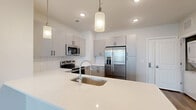 Located at 8067 Purchase Pl NE in Leland, NC, this thoughtfully designed 2-bedroom, 3-bathroom single-story home offers a clean, modern aesthetic throughout. The open-concept layout connects the kitchen and living room seamlessly, creating a bright and functional living space bathed in natural light from multiple windows. The contemporary kitchen is a standout feature, boasting gray shaker-style cabinetry, a white quartz peninsula with an undermount sink, subway tile backsplash, stainless steel appliances including a French door refrigerator, electric range, built-in microwave, and dishwasher, all accented by sleek pendant lighting overhead. Light wood-look flooring flows consistently throughout the home, enhancing the airy, cohesive feel. The spacious primary bedroom offers natural light and includes a walk-in closet with wire shelving. The second bedroom also features a closet and a bright window. Three well-appointed bathrooms include a primary bath with a large sliding glass walk-in shower, white cabinetry, and a quartz vanity. The neutral color palette, recessed lighting, and modern fixtures contribute to a clean, move-in-ready ambiance throughout this well-laid-out Leland home.