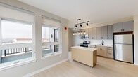 This thoughtfully designed 2-bedroom, 2-bathroom residence at 630 Kenilworth Terrace NE in Washington, DC offers a clean, contemporary aesthetic throughout its single-floor layout. Light hardwood-style flooring flows seamlessly across every room, complementing the warm neutral tones on the walls and crisp white trim and panel doors.

The open-concept kitchen and living area serves as the heart of the home. The kitchen is outfitted with stainless steel appliances, two-tone cabinetry combining gray uppers and natural wood-finish lowers, a white subway tile backsplash, light quartz countertops, and a freestanding island with additional storage. A stylish multi-pendant chandelier and track lighting illuminate the space, while large windows invite abundant natural light and city views.

Both bedrooms are well-proportioned, featuring large windows with roller shades that frame panoramic views of the Washington, DC skyline and surrounding neighborhood. The primary bedroom includes a spacious double-door closet. The two bathrooms are finished with light tile flooring, floating wood-tone vanities, white quartz countertops, and large rectangular mirrors with modern fixtures.

A connecting hallway links the bedrooms and bathrooms with recessed ceiling lighting for a polished finish. The overall ambiance is bright, modern, and move-in ready.
