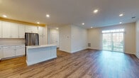 Located at 9172 New Falls Rd in Levittown, PA, this single-floor residence offers a clean, modern aesthetic with thoughtful finishes throughout. The open-concept layout connects the kitchen and living area seamlessly, creating a bright and spacious feel. Recessed lighting illuminates the entire space, complemented by natural light streaming through large windows and a glass sliding door that offers views of the surrounding outdoor greenery.

The kitchen is a standout feature, boasting crisp white shaker-style cabinetry extending to the ceiling for generous storage, a large center island with a quartz countertop and undermount sink, and a full suite of stainless steel appliances including a range, microwave, and refrigerator. Warm wood-look luxury vinyl plank flooring runs consistently throughout the main living areas and bedrooms, adding a cohesive and durable touch.

The bedrooms are well-proportioned, featuring neutral walls, recessed lighting, and ample closet space. The bathrooms are outfitted with sleek, frameless sliding glass shower enclosures with integrated grab bars, tile flooring, and clean white finishes. The overall design emphasizes a fresh, move-in-ready interior with a neutral palette that provides a versatile backdrop throughout the home.