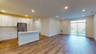 Located at 9172 New Falls Rd in Levittown, PA, this single-floor residence offers a clean, modern aesthetic with thoughtful finishes throughout. The open-concept layout connects the kitchen and living area seamlessly, creating a bright and spacious feel. Recessed lighting illuminates the entire space, complemented by natural light streaming through large windows and a glass sliding door that offers views of the surrounding outdoor greenery.

The kitchen is a standout feature, boasting crisp white shaker-style cabinetry extending to the ceiling for generous storage, a large center island with a quartz countertop and undermount sink, and a full suite of stainless steel appliances including a range, microwave, and refrigerator. Warm wood-look luxury vinyl plank flooring runs consistently throughout the main living areas and bedrooms, adding a cohesive and durable touch.

The bedrooms are well-proportioned, featuring neutral walls, recessed lighting, and ample closet space. The bathrooms are outfitted with sleek, frameless sliding glass shower enclosures with integrated grab bars, tile flooring, and clean white finishes. The overall design emphasizes a fresh, move-in-ready interior with a neutral palette that provides a versatile backdrop throughout the home.