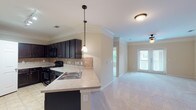 Located in Spring, TX, this single-floor residence offers a well-designed open-concept layout that seamlessly connects the kitchen and living areas. The kitchen is a standout feature, equipped with rich dark espresso cabinetry, a tile backsplash, light countertops, black appliances including a range and built-in microwave, and a peninsula with a stainless steel sink. Pendant lighting and track lighting add functional style throughout the kitchen. Tile flooring anchors the kitchen area, while plush neutral carpet extends throughout the living spaces and bedrooms. Crown molding is present throughout, adding a refined architectural detail to each room. The living room is generously proportioned and benefits from natural light, with double doors leading to an outdoor balcony. Ceiling fans are installed in the living room and bedrooms, enhancing comfort. The bedrooms are well-sized, each featuring closets and windows that allow natural light in. The bathroom includes a combined tub and shower with tile surround, dark vanity cabinetry, and light countertops. Staircase details with white balusters add a classic touch. Overall, the space presents a clean, neutral palette throughout.