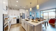 This thoughtfully designed 2-bedroom, 2.5-bathroom residence offers a seamless blend of modern aesthetics and functional living. The open-concept kitchen and living area serves as the heart of the home, anchored by a large center island with quartz countertops, pendant lighting, crisp white cabinetry reaching to the ceiling, stainless steel appliances, and a built-in wine refrigerator. Wood-look flooring runs throughout the main living areas, complementing the contemporary design. The living room is a showstopper, featuring dramatic floor-to-ceiling windows and glass sliding doors that flood the space with natural light and frame sweeping panoramic views of the surrounding cityscape and mountains. The spacious primary bedroom offers a serene retreat with plush carpeting, natural light, and access to a well-appointed en-suite bathroom complete with a glass-enclosed walk-in shower, dual vanity with modern fixtures, and tile flooring. A generously sized walk-in closet with built-in shelving provides ample storage. The second bedroom is equally well-sized, with its own bathroom access. A convenient half-bath serves guests. The dedicated laundry room includes a full-size washer, cabinetry, and a utility sink, adding practical everyday convenience to this refined residence.