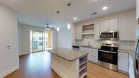Located at 305 Oberlin Rd in Raleigh, NC, this well-appointed single-floor residence offers a thoughtfully designed open-concept layout that seamlessly connects the kitchen, dining, and living areas. Warm hardwood-style flooring flows throughout the main living spaces, complemented by clean white walls and recessed lighting that create a bright, welcoming atmosphere.

The kitchen is a standout feature, showcasing crisp white shaker cabinetry extending to the ceiling, granite countertops, and a herringbone-patterned tile backsplash. A central island with built-in shelving provides additional prep space and storage. Stainless steel appliances — including a range, microwave, dishwasher, and French door refrigerator — complete the modern aesthetic. Elegant pendant lighting hangs above the island, adding a refined touch.

The living area is anchored by a ceiling fan and large sliding glass doors that open to a private balcony, filling the space with natural light and outdoor views. An in-unit stacked washer and dryer adds everyday convenience.

The bathroom is finished with a granite-topped white vanity, a framed mirror, wood-look tile flooring, and a walk-in shower with white subway tile and brushed gold hardware. A spacious walk-in closet with multi-level shelving and hanging rods provides ample storage. This residence combines contemporary finishes with functional design throughout.