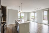 This modern single-floor residence offers a thoughtfully designed open-concept layout that seamlessly connects the kitchen, dining, and living areas. The kitchen is a standout feature, outfitted with rich dark wood cabinetry, a full suite of stainless steel appliances including a refrigerator, microwave, and range, and a central island with a light quartz countertop and undermount sink — ideal for both meal preparation and casual dining. Pendant lighting adds a warm, stylish touch above the island, complemented by track lighting in the living area. Wide-plank light wood flooring runs throughout the entire residence, lending warmth and continuity to the space. The expansive living area is bathed in natural light, courtesy of large floor-to-ceiling windows with wood-framed accents that frame sweeping outdoor views of the surrounding neighborhood. The bedrooms continue the bright, airy aesthetic with generous window presence and clean neutral walls. Two bathrooms are finished with large-format tile in soft neutral tones — one featuring a soaking tub with shower combination and chrome fixtures, the other a glass-enclosed walk-in shower stall. The overall ambiance is clean, contemporary, and move-in ready.