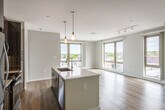 This modern single-floor residence offers a thoughtfully designed open-concept layout that seamlessly connects the kitchen, dining, and living areas. The kitchen is a standout feature, outfitted with rich dark wood cabinetry, a full suite of stainless steel appliances including a refrigerator, microwave, and range, and a central island with a light quartz countertop and undermount sink — ideal for both meal preparation and casual dining. Pendant lighting adds a warm, stylish touch above the island, complemented by track lighting in the living area. Wide-plank light wood flooring runs throughout the entire residence, lending warmth and continuity to the space. The expansive living area is bathed in natural light, courtesy of large floor-to-ceiling windows with wood-framed accents that frame sweeping outdoor views of the surrounding neighborhood. The bedrooms continue the bright, airy aesthetic with generous window presence and clean neutral walls. Two bathrooms are finished with large-format tile in soft neutral tones — one featuring a soaking tub with shower combination and chrome fixtures, the other a glass-enclosed walk-in shower stall. The overall ambiance is clean, contemporary, and move-in ready.