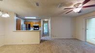 This single-floor residence offers a functional and comfortable layout across two bedrooms and two bathrooms. The open-concept living area is spacious and carpeted, featuring a ceiling fan overhead and a textured ceiling. A sliding glass door allows natural light to fill the room, creating a bright and airy atmosphere.

The kitchen is positioned adjacent to the living area, separated by a breakfast bar countertop that provides a casual dining option. Warm-toned wood cabinetry lines the walls, complemented by stainless steel appliances including a refrigerator and an electric range. Wood-look flooring adds a practical, easy-to-maintain surface underfoot.

A hallway connects the main living space to the bedrooms, both of which are carpeted and well-proportioned. One bedroom features a large window with views of surrounding greenery, offering a serene setting. Each bedroom includes door access to closets or additional storage.

The two bathrooms are consistent in design, each featuring wood-toned vanity cabinetry, a single-basin sink with a large mirror, and wood-look flooring. One bathroom includes a tiled tub-shower combination, while the second serves as a more compact full bath. Together, the rooms create a cohesive, neutral-toned living environment throughout.