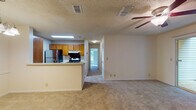 This single-floor residence offers a functional and comfortable layout across two bedrooms and two bathrooms. The open-concept living area is spacious and carpeted, featuring a ceiling fan overhead and a textured ceiling. A sliding glass door allows natural light to fill the room, creating a bright and airy atmosphere.

The kitchen is positioned adjacent to the living area, separated by a breakfast bar countertop that provides a casual dining option. Warm-toned wood cabinetry lines the walls, complemented by stainless steel appliances including a refrigerator and an electric range. Wood-look flooring adds a practical, easy-to-maintain surface underfoot.

A hallway connects the main living space to the bedrooms, both of which are carpeted and well-proportioned. One bedroom features a large window with views of surrounding greenery, offering a serene setting. Each bedroom includes door access to closets or additional storage.

The two bathrooms are consistent in design, each featuring wood-toned vanity cabinetry, a single-basin sink with a large mirror, and wood-look flooring. One bathroom includes a tiled tub-shower combination, while the second serves as a more compact full bath. Together, the rooms create a cohesive, neutral-toned living environment throughout.