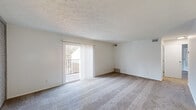 Located at 500 Valley Brook Dr in Milford, Ohio, this single-floor residence offers a straightforward and functional layout designed for comfortable everyday living. The spacious living area serves as the heart of the home, featuring wall-to-wall carpeting, neutral white walls, and a textured ceiling that adds subtle visual interest. A standout feature of the living room is the painted brick accent wall, which lends a touch of character and warmth to the otherwise clean, minimalist space. A sliding glass door opens directly onto a private balcony, allowing natural light to fill the room and providing views of the surrounding outdoor setting. The bedroom areas continue the same carpeted flooring and neutral palette, each benefiting from individual windows fitted with blinds that invite soft, natural light while maintaining privacy. The bathroom is neatly appointed with a full tub and shower combination, a single vanity with a sink, and a wall-mounted mirror, all finished in crisp white tones for a clean, functional feel. Throughout the residence, the consistent use of neutral colors and plush carpeting creates a cohesive, calm ambiance. The layout flows efficiently between living, sleeping, and utility spaces, making this a well-organized and practical home in the Milford, Ohio community.