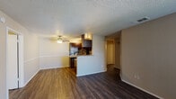 This single-story residence features a cohesive, open layout with dark hardwood-style flooring running throughout. The living area is generously proportioned, anchored by a fireplace and complemented by a ceiling fan overhead. Natural light enters through blinded windows, lending a bright, airy quality to the space. A dedicated dining area sits adjacent to the kitchen, also equipped with a ceiling fan and defined by a chair-rail detail along the neutral-toned walls.

The kitchen is designed as a galley-style space with dark espresso cabinetry, granite-look countertops, and a mosaic tile backsplash that adds visual texture. A breakfast bar peninsula opens the kitchen toward the dining and living areas, enhancing the flow between spaces. Stainless steel appliances, including a refrigerator, electric range, microwave, and dishwasher, complete the kitchen's functional layout. Track lighting provides focused illumination throughout.

The bedrooms continue the hardwood-style flooring and each include ceiling fans and windows. The bathrooms feature dark-framed vanity mirrors, granite-look counters, dark cabinetry, and tiled tub-shower combinations. A textured popcorn ceiling is consistent throughout, contributing to the unit's overall character.