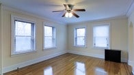 This single-floor space showcases classic architectural details and a warm, inviting ambiance. The main room is highlighted by polished hardwood floors that reflect natural light beautifully, creating a bright and airy atmosphere. Four windows fitted with horizontal blinds line two walls, allowing generous amounts of daylight to fill the room while offering privacy control. Crown molding frames the ceiling elegantly, adding a refined, traditional character to the space. A ceiling fan with integrated lighting is centrally positioned, providing both functional air circulation and supplemental illumination. The walls are finished in a soft, neutral tone that complements the warm wood flooring and enhances the overall sense of openness. Wide baseboards throughout add to the classic aesthetic. The open layout and corner placement of the windows make the room feel expansive and versatile, suitable for a variety of uses. The combination of natural light, traditional detailing, and well-maintained hardwood flooring gives this space a timeless appeal that is both practical and visually pleasing.