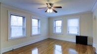 This single-floor space showcases classic architectural details and a warm, inviting ambiance. The main room is highlighted by polished hardwood floors that reflect natural light beautifully, creating a bright and airy atmosphere. Four windows fitted with horizontal blinds line two walls, allowing generous amounts of daylight to fill the room while offering privacy control. Crown molding frames the ceiling elegantly, adding a refined, traditional character to the space. A ceiling fan with integrated lighting is centrally positioned, providing both functional air circulation and supplemental illumination. The walls are finished in a soft, neutral tone that complements the warm wood flooring and enhances the overall sense of openness. Wide baseboards throughout add to the classic aesthetic. The open layout and corner placement of the windows make the room feel expansive and versatile, suitable for a variety of uses. The combination of natural light, traditional detailing, and well-maintained hardwood flooring gives this space a timeless appeal that is both practical and visually pleasing.