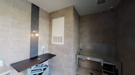 Located at 1930 Kingsley Dr in Pearland, Texas, this single-floor pet grooming facility is purpose-built for professional pet care. The space is finished with large-format neutral stone-toned ceramic tile covering both the floors and walls from floor to ceiling, creating a clean, hygienic, and visually cohesive environment throughout.

The grooming area is equipped with a hydraulic lift grooming table, allowing for adjustable working heights to accommodate pets of varying sizes. A stainless steel wash station with an integrated stair step for pet access is positioned nearby, paired with a professional handheld sprayer — providing a fully functional bathing setup. A stainless steel utility table offers additional workspace for supplies and tools. Accent tile strips in a dark linear mosaic pattern add a design element to the otherwise neutral palette.

The space benefits from large floor-to-ceiling windows that bring in generous natural light and offer views of an outdoor pool and landscaped common area. A glass-paneled exterior door provides easy access. Climate control is handled through a built-in HVAC vent, ensuring a comfortable environment for both pets and groomers. The combination of durable finishes, professional equipment, and thoughtful design makes this a well-appointed and highly functional grooming suite.