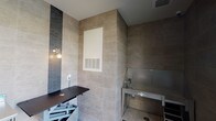 Located at 1930 Kingsley Dr in Pearland, Texas, this single-floor pet grooming facility is purpose-built for professional pet care. The space is finished with large-format neutral stone-toned ceramic tile covering both the floors and walls from floor to ceiling, creating a clean, hygienic, and visually cohesive environment throughout.

The grooming area is equipped with a hydraulic lift grooming table, allowing for adjustable working heights to accommodate pets of varying sizes. A stainless steel wash station with an integrated stair step for pet access is positioned nearby, paired with a professional handheld sprayer — providing a fully functional bathing setup. A stainless steel utility table offers additional workspace for supplies and tools. Accent tile strips in a dark linear mosaic pattern add a design element to the otherwise neutral palette.

The space benefits from large floor-to-ceiling windows that bring in generous natural light and offer views of an outdoor pool and landscaped common area. A glass-paneled exterior door provides easy access. Climate control is handled through a built-in HVAC vent, ensuring a comfortable environment for both pets and groomers. The combination of durable finishes, professional equipment, and thoughtful design makes this a well-appointed and highly functional grooming suite.