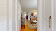 This single-floor residence offers a thoughtfully designed layout that balances comfort and functionality. The entry, framed by classic glass-paned French doors, opens onto warm hardwood flooring that flows throughout the main living areas, establishing a cohesive and inviting aesthetic.

The living room is a bright, comfortable space accented by crown molding, soft gray walls, and natural light from nearby windows. A marble-top coffee table, patterned area rug, and coordinated artwork lend the room a polished, curated character.

The bedroom features the same rich hardwood floors and crown molding, with ample natural light filtering through large windows dressed with decorative valances. A metal-frame bed and classic nightstands complete the well-proportioned room.

The galley kitchen is efficiently arranged, offering rich wood cabinetry, dark granite countertops, tile flooring, and a full suite of black appliances including a gas range and built-in microwave. A window above the sink brings in natural light, and a small breakfast bar provides additional functionality.

The bathroom is finished with classic white subway tile, a decorative mosaic border, a soaking tub with shower, and a pedestal-style vanity — clean and timeless in design. Overall, the space presents a cohesive, warm ambiance with consistent classic detailing throughout.