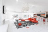 Located at 275 Fieldcrest St in Ann Arbor, Michigan, this striking single-floor commercial space combines bold contemporary design with an open, welcoming atmosphere. The layout flows seamlessly from a clean, modern reception and entry area — outfitted with pendant lighting, a service counter, and a colorful bottle display wall — into a spacious main lounge.

The lounge serves as the centerpiece of the space, featuring soaring vaulted ceilings, gleaming white tile floors, and an abundance of natural light streaming through large windows and an arched window overlooking lush greenery. A dramatic stone-clad fireplace anchors one wall, topped with a mounted flat-screen display, while an arched accent wall and woven globe pendant chandeliers add architectural character overhead.

Bold red curved sectional seating contrasts sharply against the crisp all-white interior palette, complemented by a patterned area rug and modern accent chairs. A white baby grand piano occupies a dedicated corner, lending an elegant and artistic touch to the space.

A built-in bar area with colorful bottle shelving and red bar stools provides a vibrant hospitality feature, ideal for gatherings and events. Throughout, recessed lighting and carefully selected furnishings contribute to a polished, upscale ambiance that is both functional and visually dynamic.