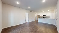 This single-story residence at Wimbledon Loop in Little Rock, Arkansas, offers a well-designed open-concept layout that seamlessly connects the living area and kitchen. Dark hardwood-style flooring runs throughout the main living spaces, providing a rich, grounded aesthetic that contrasts cleanly with the bright white walls and recessed lighting overhead.

The kitchen is a functional centerpiece of the unit, featuring white shaker-style cabinetry extending to the ceiling for ample storage, granite-look countertops, and a full suite of stainless steel appliances including a refrigerator, range, and microwave. A peninsula with a double-basin sink and pendant lighting above adds both workspace and a casual dining option, while maintaining visual openness to the living area.

The living space is generously sized with recessed lighting and a set of French doors that introduce natural light and provide outdoor access. The bedroom is carpeted for comfort, fitted with a ceiling fan, and accompanied by a walk-in closet with wire shelving. The bathroom continues the clean aesthetic with white cabinetry, granite-look countertops, a large vanity mirror, and consistent flooring throughout.