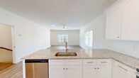 This two-story home in Athens, Georgia offers a clean, modern design across four bedrooms and three bathrooms. The main level features an open-concept kitchen and living room with warm hardwood-style flooring, white shaker cabinetry, granite countertops, a stainless steel undermount sink, subway tile backsplash, and stainless steel appliances including a range, microwave, and dishwasher. A peninsula island provides additional workspace and casual seating. The living area is bright and airy, with multiple windows framing outdoor greenery and a ceiling fan overhead. Each of the three bathrooms continues the cohesive design language with granite-topped white vanities, undermount sinks, brushed nickel fixtures, and tub-shower combinations. The bedrooms are generously proportioned, finished with the same hardwood-style flooring, ceiling fans, and large windows that fill each room with natural light. The primary bedroom is well-sized and features walk-in closet access with wire shelving. Additional storage is provided throughout the home, including a dedicated hallway closet. The second floor mirrors the first in square footage, offering a balanced, functional layout. A neutral color palette of crisp whites and warm wood tones gives the entire home a fresh, move-in ready aesthetic.