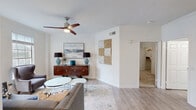 This single-floor residence offers a thoughtfully designed layout that balances comfort and functionality. The living area is bright and welcoming, featuring light hardwood-style flooring, crown molding, and a contemporary ceiling fan. Large windows flood the space with natural light, while a built-in niche with granite countertop adds a distinctive architectural touch. The open-concept kitchen is outfitted with crisp white shaker cabinetry, granite countertops, a classic subway tile backsplash, and a full suite of stainless steel appliances, including a refrigerator, range, and over-the-range microwave. An adjacent dining area provides ample space for entertaining. The primary bedroom is generously proportioned with plush carpeting, a ceiling fan, natural light from exterior windows, and direct access to a private en-suite bathroom. A walk-in closet offers excellent storage. Additional bedrooms continue the home's clean, neutral aesthetic. The bathroom features a tiled tub-and-shower combination with brushed nickel fixtures and wood-look flooring. Throughout the residence, a consistent palette of whites and warm neutrals creates a calm, cohesive ambiance suitable for a variety of lifestyles.